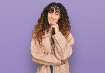 Young hispanic girl wearing winter clothes looking confident at the camera with smile with crossed arms and hand raised on chin. thinking positive.