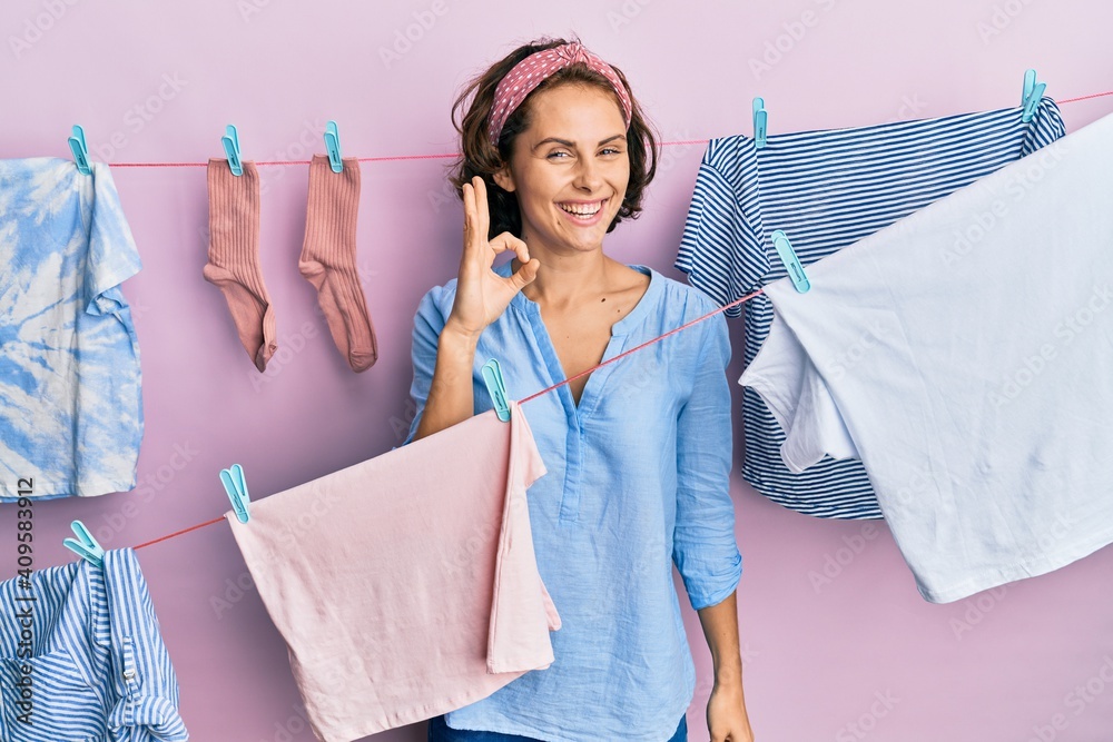 Sticker young brunette woman doing laundry around string hangs smiling positive doing ok sign with hand and 