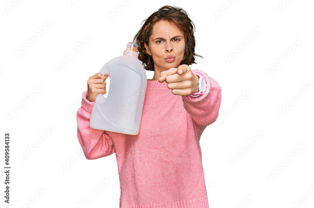 Sticker Young hispanic woman doing laundry holding detergent bottle pointing with finger to the camera and to you, confident gesture looking serious