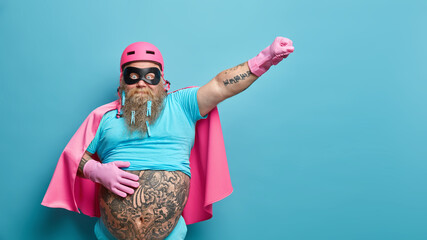 Surprised bearded man dressed like superhero stretches arm as if going to fly keeps hand on big...