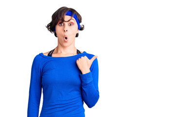 Beautiful young woman with short hair wearing training workout clothes surprised pointing with hand finger to the side, open mouth amazed expression.