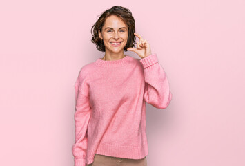 Young hispanic woman wearing casual clothes smiling and confident gesturing with hand doing small size sign with fingers looking and the camera. measure concept.