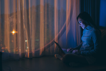 A beautiful young woman using and working on laptop computer with bright light screen in the late night at home