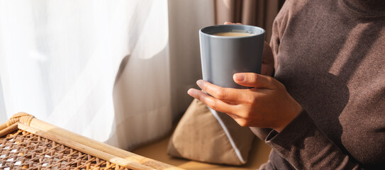 Closeup image of a woman holding and drinking hot coffee at home in the morning