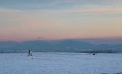 Deerstand on a snowy field during dusk with mountains in the background