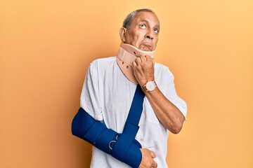 Handsome mature senior man wearing cervical collar and arm on sling with hand on chin thinking...