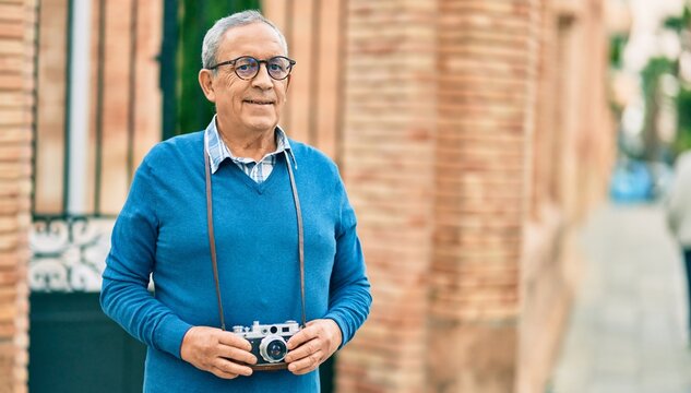 Senior grey-haired tourist man smiling happy using vintage camera at the city.