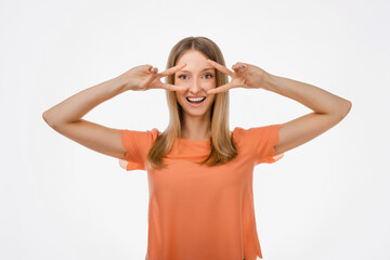 Portrait of optimistic blond girl showing peace sign over eye and smiling, white background. Just be cool about it