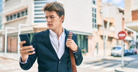 Young caucasian businessman with serious expression using smartphone at the city.