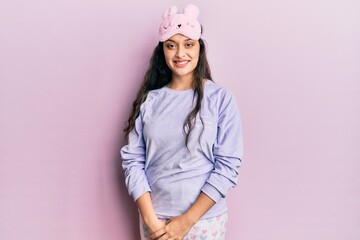 Beautiful middle eastern woman wearing sleep mask and pajama looking positive and happy standing and smiling with a confident smile showing teeth