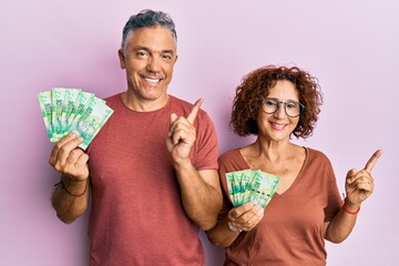 Beautiful middle age couple holding south african 10 rand banknotes smiling happy pointing with hand and finger to the side