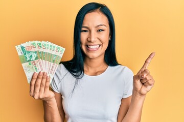 Beautiful hispanic woman holding hong kong 50 dollars banknotes smiling happy pointing with hand and finger to the side