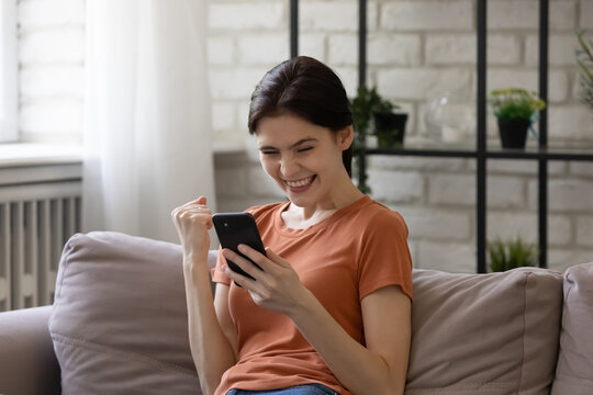 Overjoyed woman looking at phone screen, celebrating success, showing yes gesture, excited satisfied young female holding smartphone, reading good news in message, lottery win, shopping offer