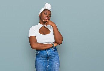 Young african woman with turban wearing hair turban over isolated background with hand on chin thinking about question, pensive expression. smiling with thoughtful face. doubt concept.