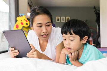 mother and her son using digital tablet in a bed at home. The use of concept of new generation, family, parenthood, authenticity, connection, technology.