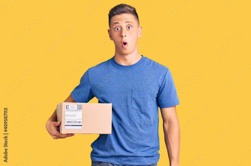 Canvas Prints Young handsome hispanic man holding delivery package scared and amazed with open mouth for surprise, disbelief face