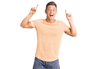 Young handsome man wearing casual clothes smiling amazed and surprised and pointing up with fingers and raised arms.