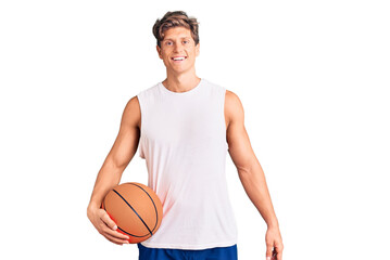 Young handsome man holding basketball ball looking positive and happy standing and smiling with a confident smile showing teeth