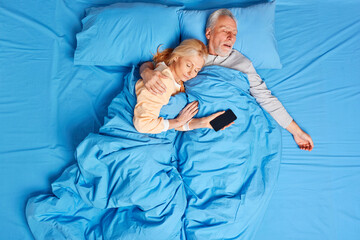 Recovery time concept. Retired woman and man in nightwear sleep deeply in bed embrace and love each...