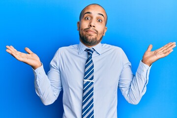 Hispanic adult man wearing business shirt and tie clueless and confused with open arms, no idea and doubtful face.