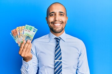 Hispanic adult man holding australian dollars looking positive and happy standing and smiling with a confident smile showing teeth