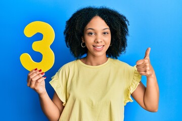 Young african american girl holding number three smiling happy and positive, thumb up doing excellent and approval sign