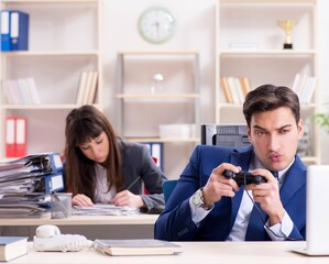 Man playing games in office while colleague is busy