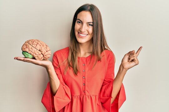 Young beautiful woman holding brain smiling happy pointing with hand and finger to the side