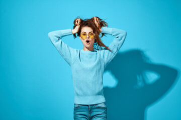 beautiful woman in blue sweater yellow sunglasses smile holding hair studio blue background