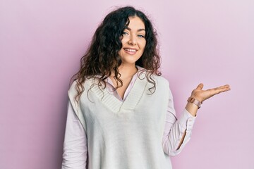 Young brunette woman with curly hair wearing casual clothes smiling cheerful presenting and pointing with palm of hand looking at the camera.