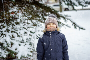 winter portrait of cute caucasian 6 years old boy in knit hat with pompom near snowy tree