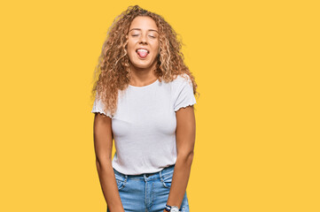 Beautiful caucasian teenager girl wearing casual white tshirt sticking tongue out happy with funny expression. emotion concept.