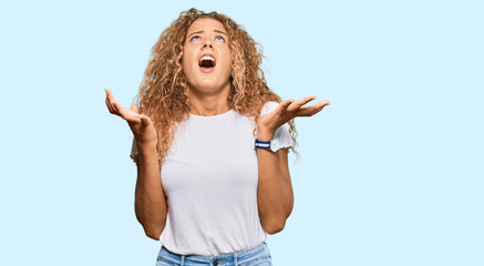 Beautiful caucasian teenager girl wearing casual white tshirt crazy and mad shouting and yelling...