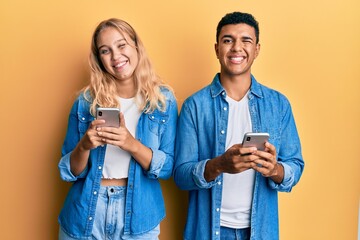 Young interracial couple using smartphone winking looking at the camera with sexy expression,...