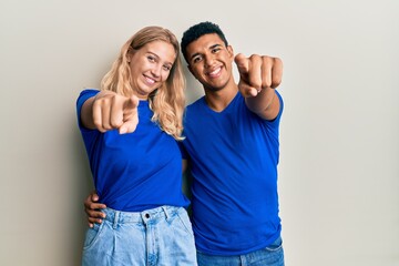 Young interracial couple wearing casual clothes pointing to you and the camera with fingers, smiling positive and cheerful