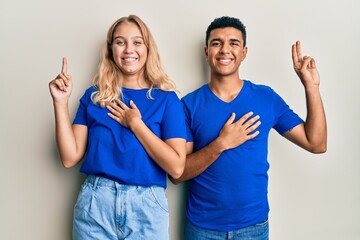 Young interracial couple wearing casual clothes smiling swearing with hand on chest and fingers up,...