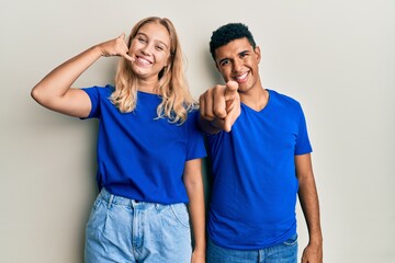 Young interracial couple wearing casual clothes smiling doing talking on the telephone gesture and pointing to you. call me.