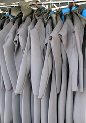 Line of multiple hanging wetsuits at surfing center.