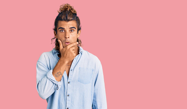 Young hispanic man wearing summer style looking fascinated with disbelief, surprise and amazed expression with hands on chin