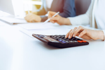 Accountant checking financial statement or counting by calculator income for tax form, hands closeup. Business woman sitting and working with colleague at the desk in office. Tax and Audit concept - obrazy, fototapety, plakaty