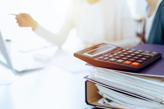 Calculator and binders with papers are waiting to be processed by business woman or bookkeeper working at the desk in office back in blur. Internal Audit and tax concept