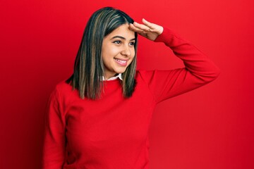 Young latin woman wearing casual clothes very happy and smiling looking far away with hand over head. searching concept.