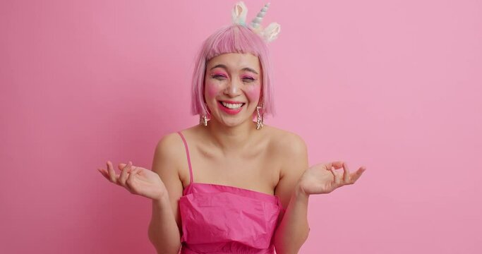 Pretty woman wears pink hair wig points at herself asks why me then laughs happily feels very happy hears very funny anecdote wears stylish dress isolated over pink background. Emotions concept
