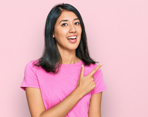 Beautiful asian young woman wearing casual pink t shirt cheerful with a smile of face pointing with hand and finger up to the side with happy and natural expression on face