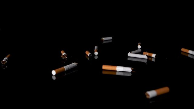 Slow-motion fall of cigarettes butts on black mirroring surface, studio-shot.
