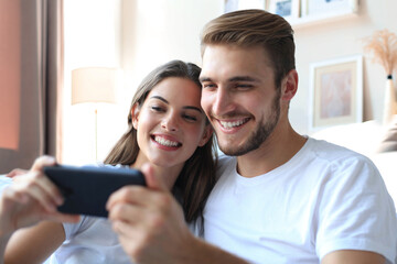 Happy couple enjoying media content in a smart phone sitting on a couch at home.