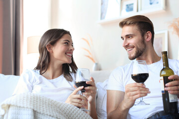 Young loving couple drinking a glass of red wine in their living room.
