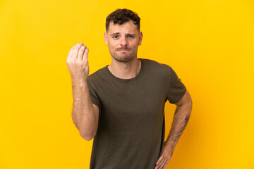 Young caucasian handsome man isolated on yellow background making Italian gesture