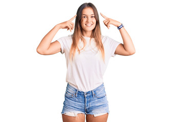 Beautiful caucasian woman wearing casual white tshirt smiling pointing to head with both hands finger, great idea or thought, good memory