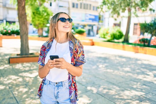 Young beautiful blonde caucasian woman smiling happy outdoors on a sunny day using smartphone